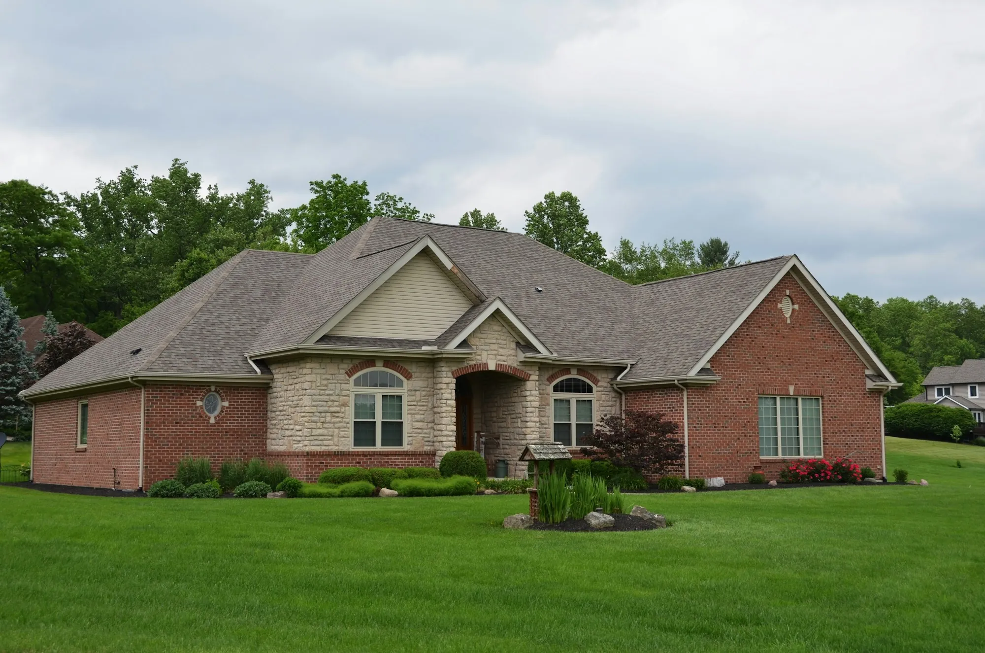 Brick and stone single-story home with a wide green lawn